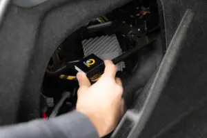 Close up image of a hand placing a small GPS tracking device into a car